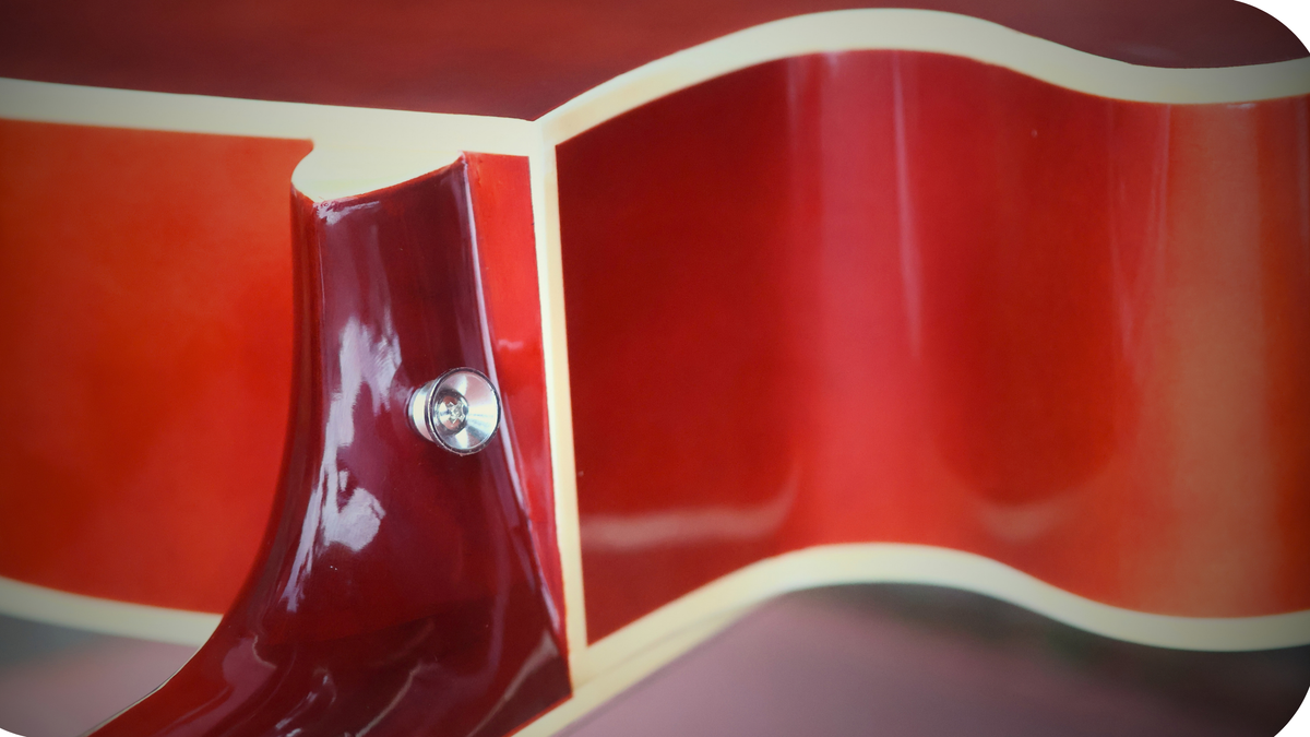 Close-up of the chrome strap button mounted on the neck heel of a black acoustic guitar body